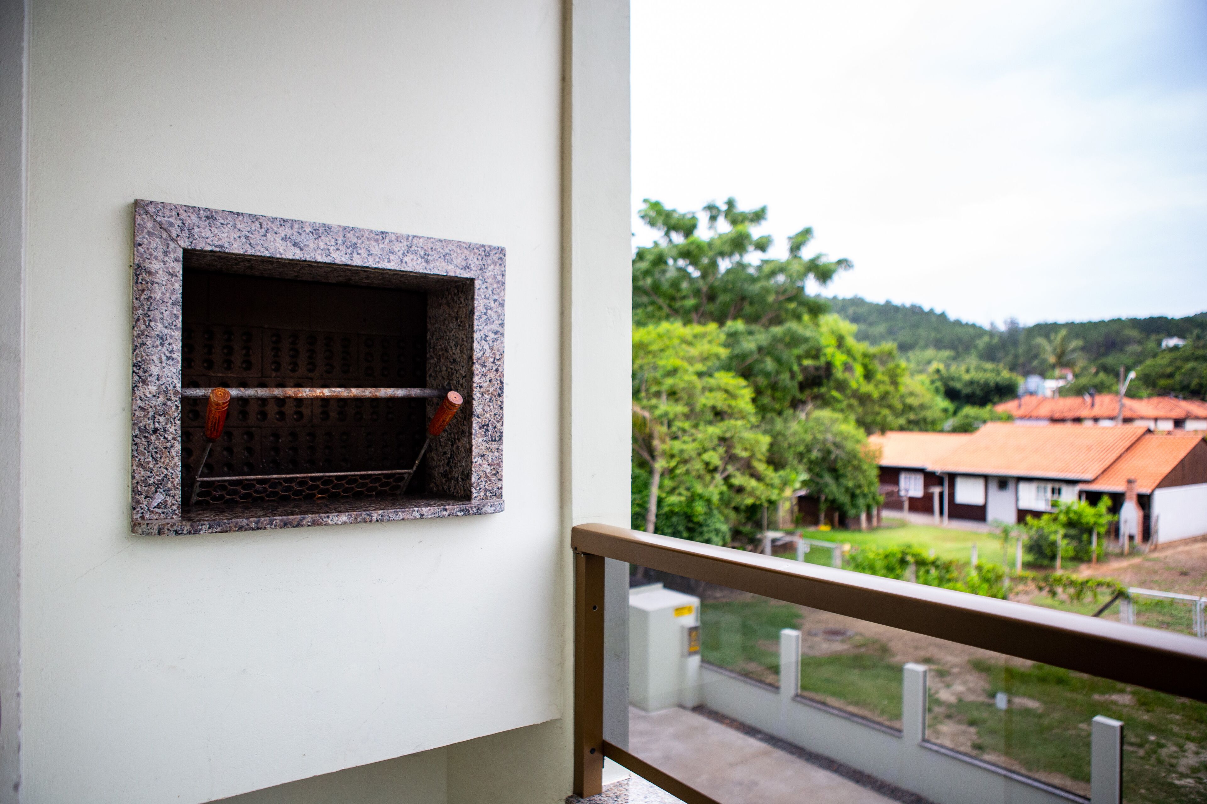 A balcony with a metal grill window, a view of a residential area with houses and greenery.