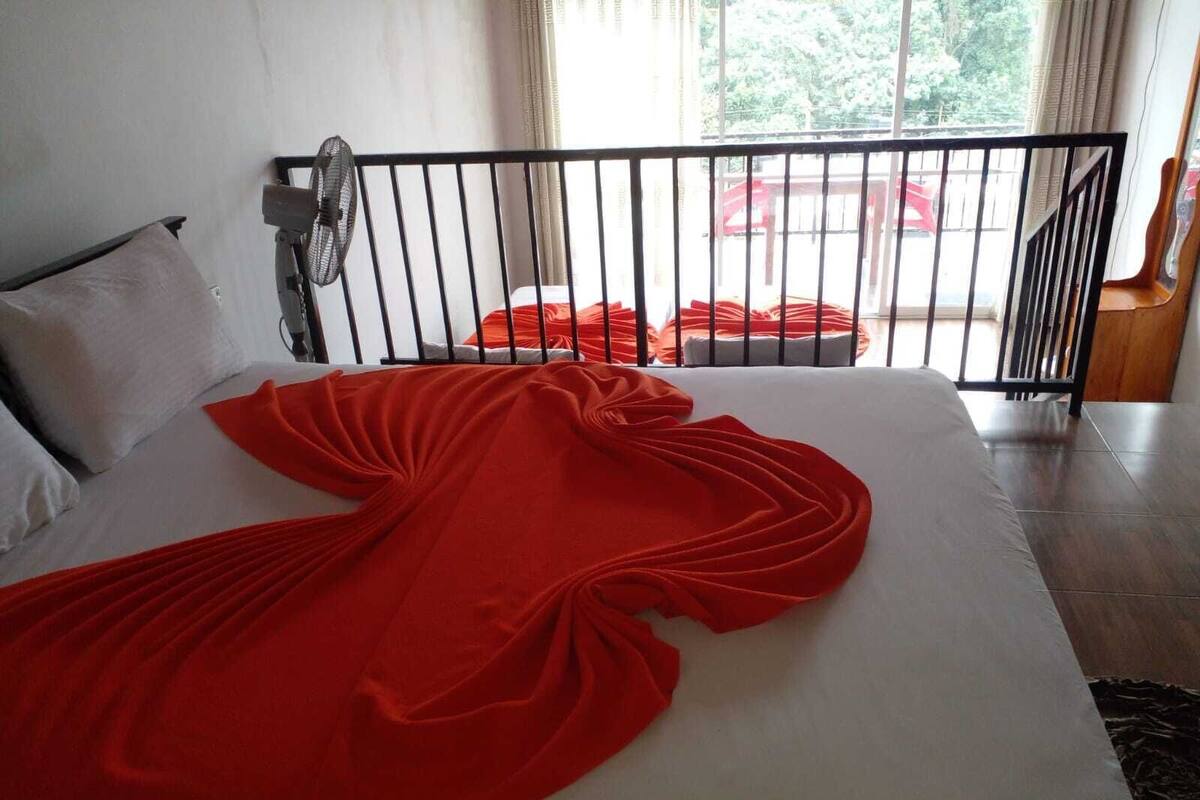A bed with a white mattress and a red blanket, a black metal headboard, and a window with curtains.