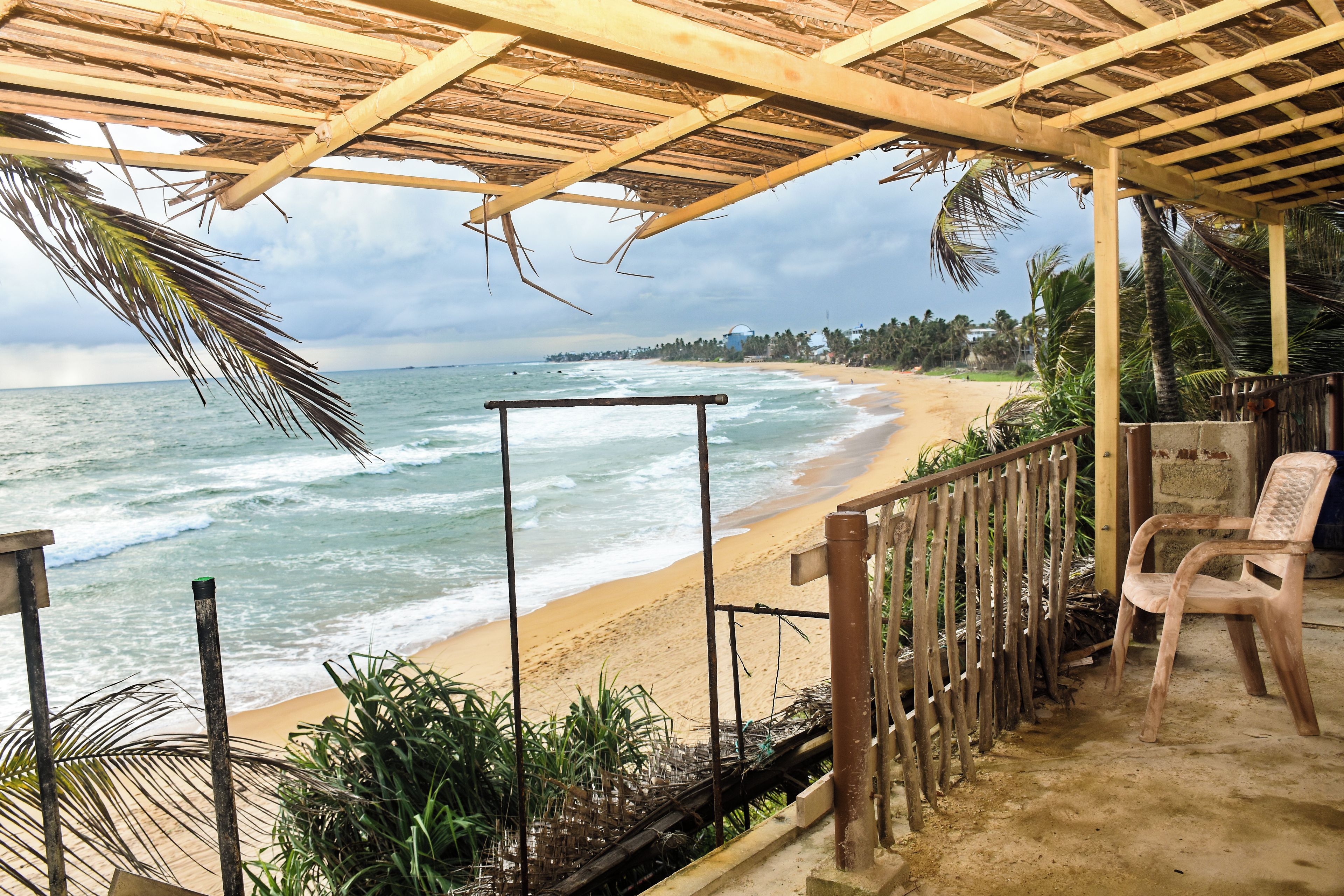 A beach view from a covered area with a wooden structure, a metal railing, and a plastic chair.