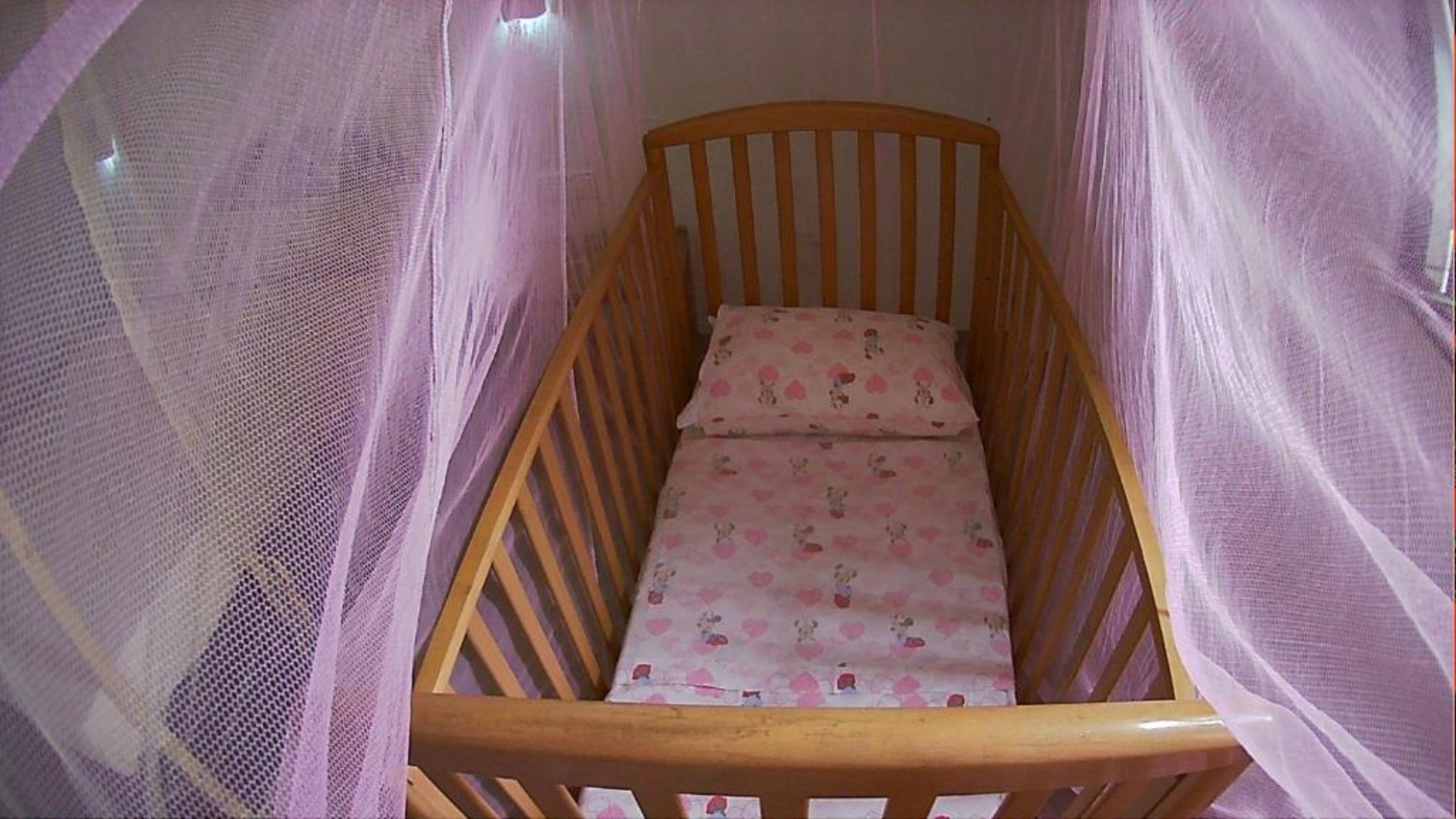 Una cuna de madera con una sábana rosa y un cojín con estampado floral.