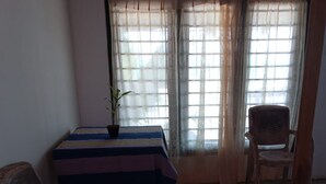 A room with a table covered by a striped tablecloth, two wicker chairs, a potted plant, and a window with sheer curtains. - villa crocodile beach (Hikkaduwa)