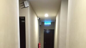 A narrow, well-lit hallway with a fire extinguisher mounted on the wall, a sign indicating a room or area, and a door at the end. - Tey Hotel (Pasir Gudang)