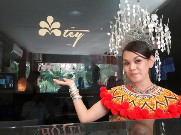 A person in traditional attire with a decorative headdress, standing in front of a hotel sign.