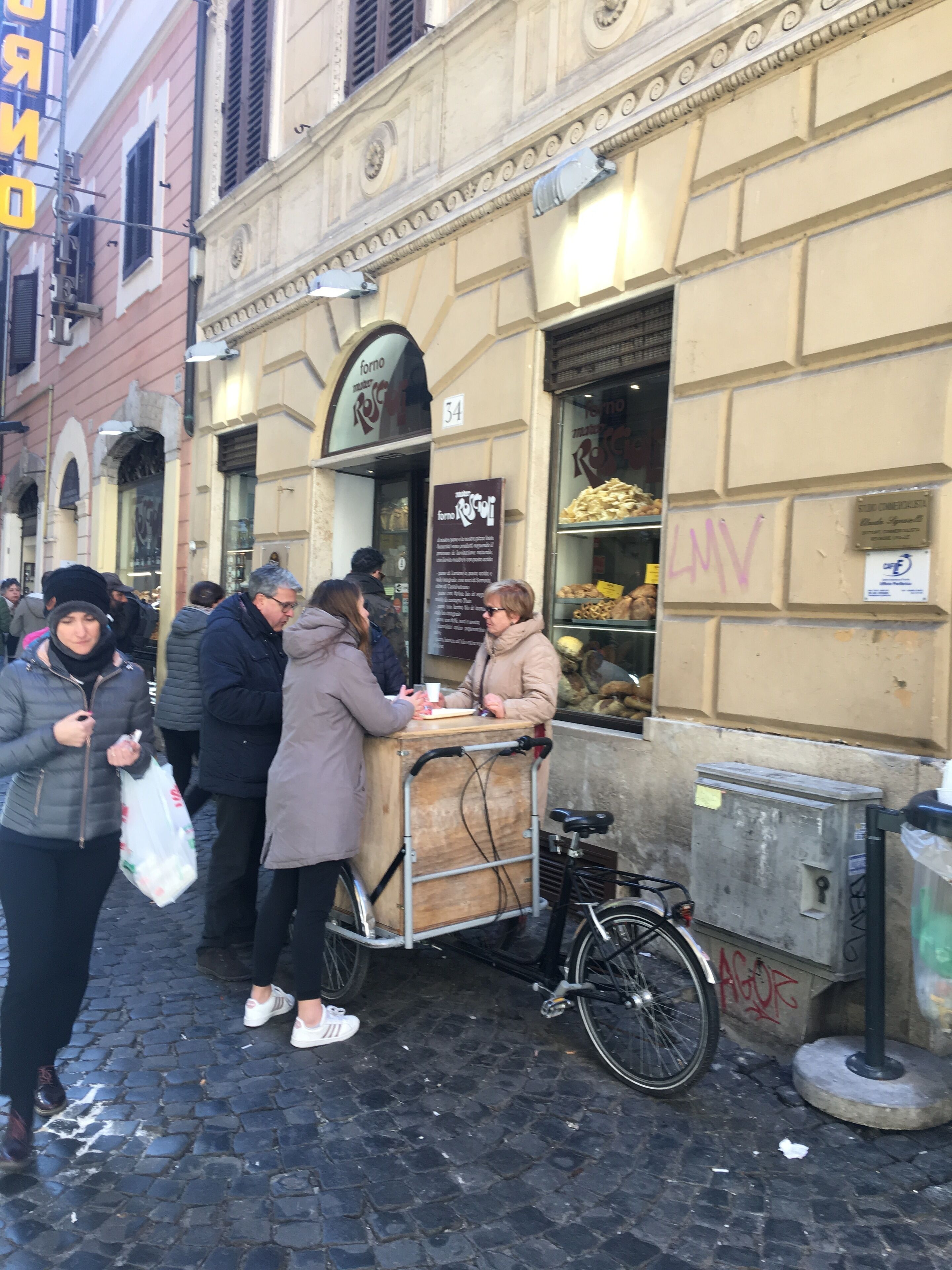 Un stand de vente de nourriture de rue est installé devant un bâtiment sur lequel est apposée une enseigne indiquant « forno ».