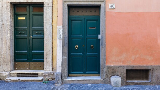 Dos puertas verdes con aldabillas de bronce, un buzón y un cartel con el número 46 en la fachada de un edificio.