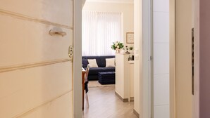 Un pasillo que conduce a una sala de estar con un sofá de color oscuro y una mesita con un jarrón de flores.