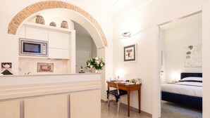 Un dormitorio moderno con una cama, un escritorio con una silla, un microondas y un jarrón decorativo.