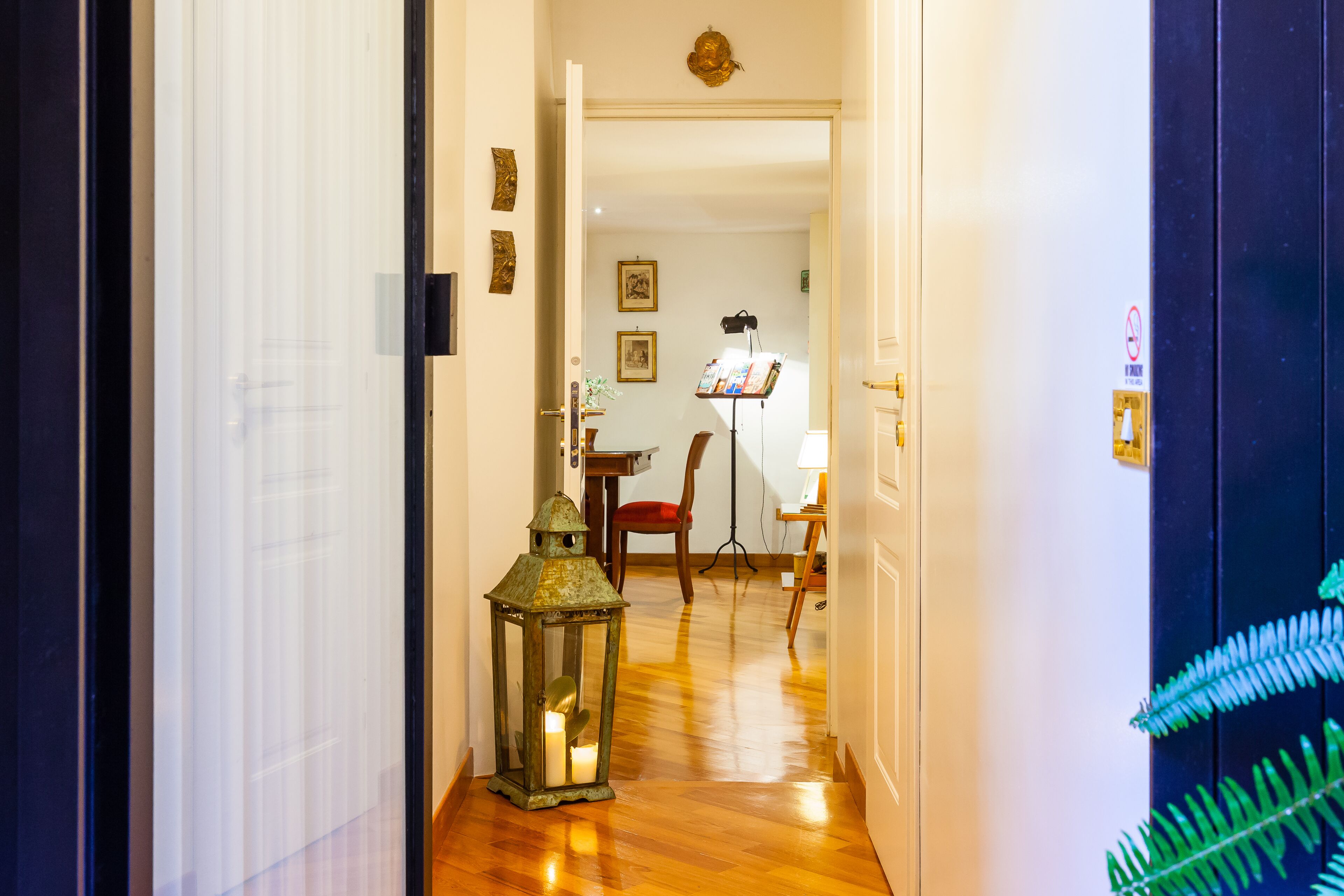 A hallway with a wooden floor, a green lantern, a chair, and a music stand with sheet music.