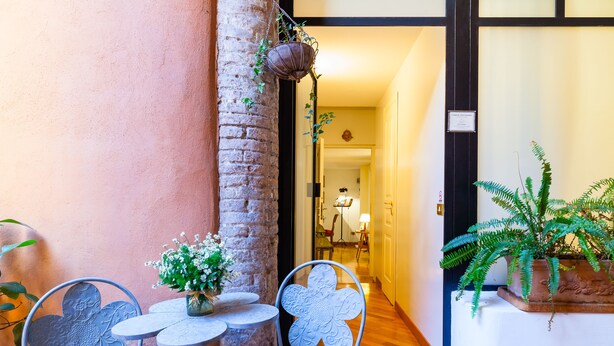 A cozy outdoor seating area with metal chairs and tables, a brick pillar, and potted plants. -  Rome center Campo de Fiori great reviews within walking distance to everything! (Roma)