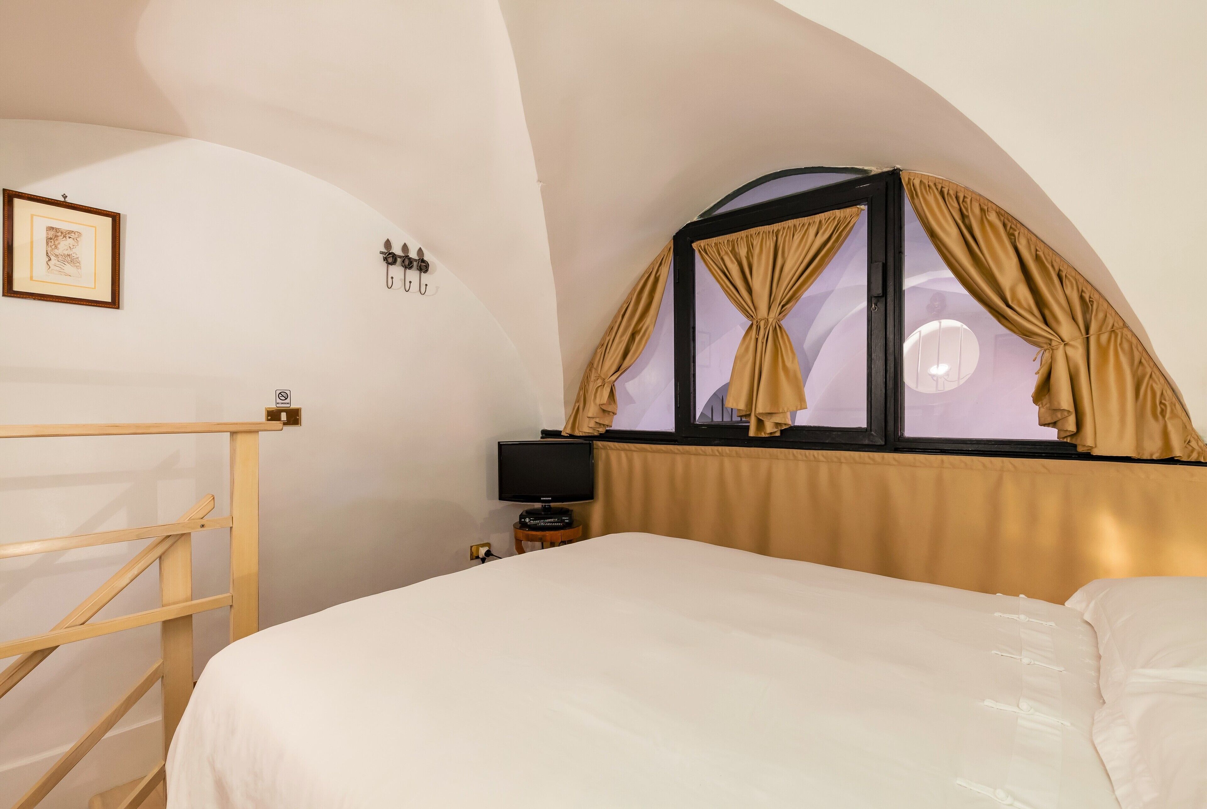 A bedroom with a bed, a wooden ladder, a television, and a window with curtains.
