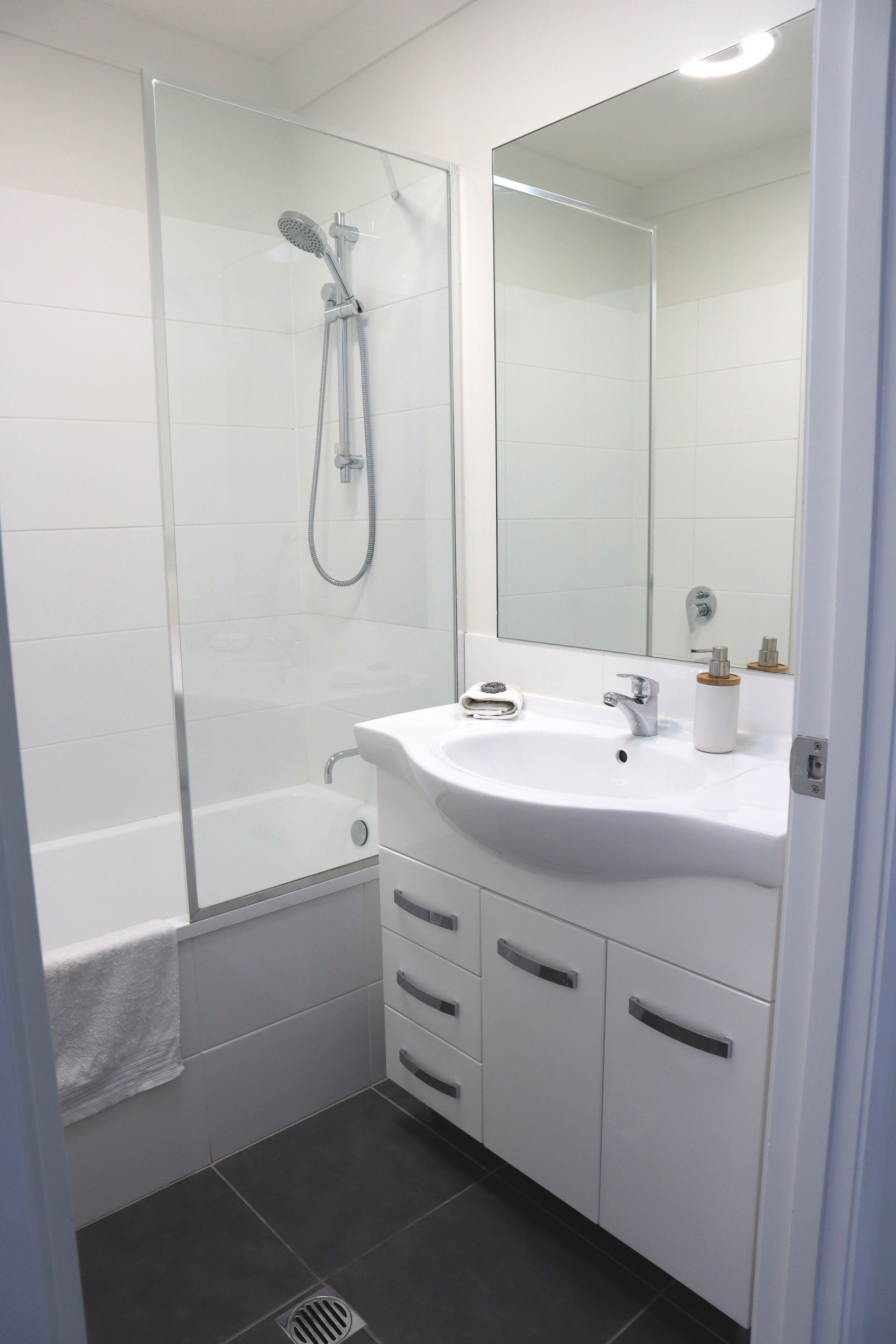 Ein modernes Badezimmer mit einer in Glas eingefassten Dusche, einem weißen Waschbecken und einem großen Spiegel.