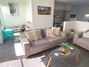 A living room with a sofa, a coffee table, a small table with a plant, and a painting of a cityscape on the wall. - Modern, stylish townhouse with pool access! (Mango Hill)