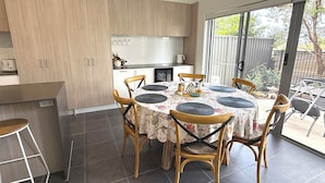 Eine moderne Küche mit Holzausstattung, ein Essbereich mit rundem Tisch und Stühlen sowie eine Glastür, die auf eine Terrasse führt.
