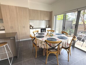 A modern kitchen with wooden cabinets, a dining area with a round table and chairs, and a sliding glass door leading to a patio. - Modern, stylish townhouse with pool access! (Mango Hill)