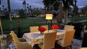 An outdoor patio with a table set for dining, surrounded by chairs, a lamp, and a grill. - Spectacular, South Facing, 4 golf cart, upgraded 2 kings+den with queen  bed. (palm desert)