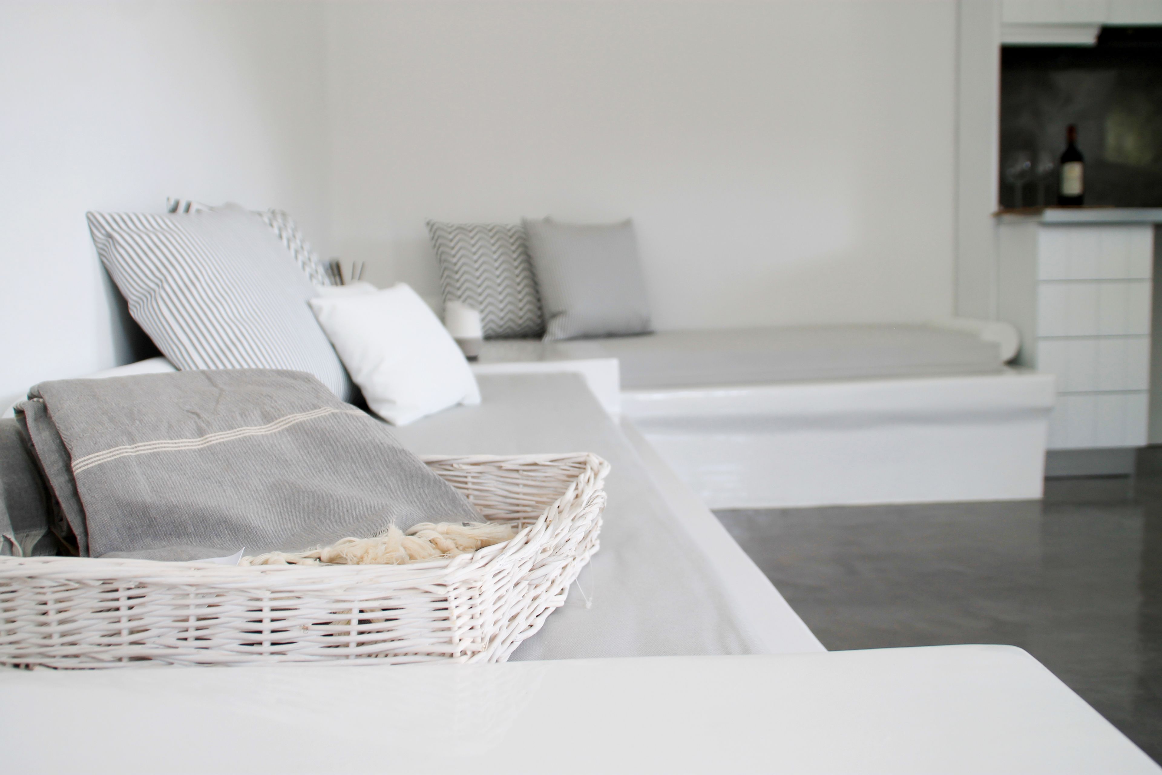 Un dormitorio moderno y minimalista con una cama blanca, almohadas grises y blancas, y una cesta de mimbre sobre la cama.