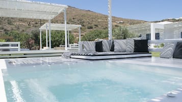 Zona de piscina con una pérgola blanca, sillones de descanso y vistas a una colina.