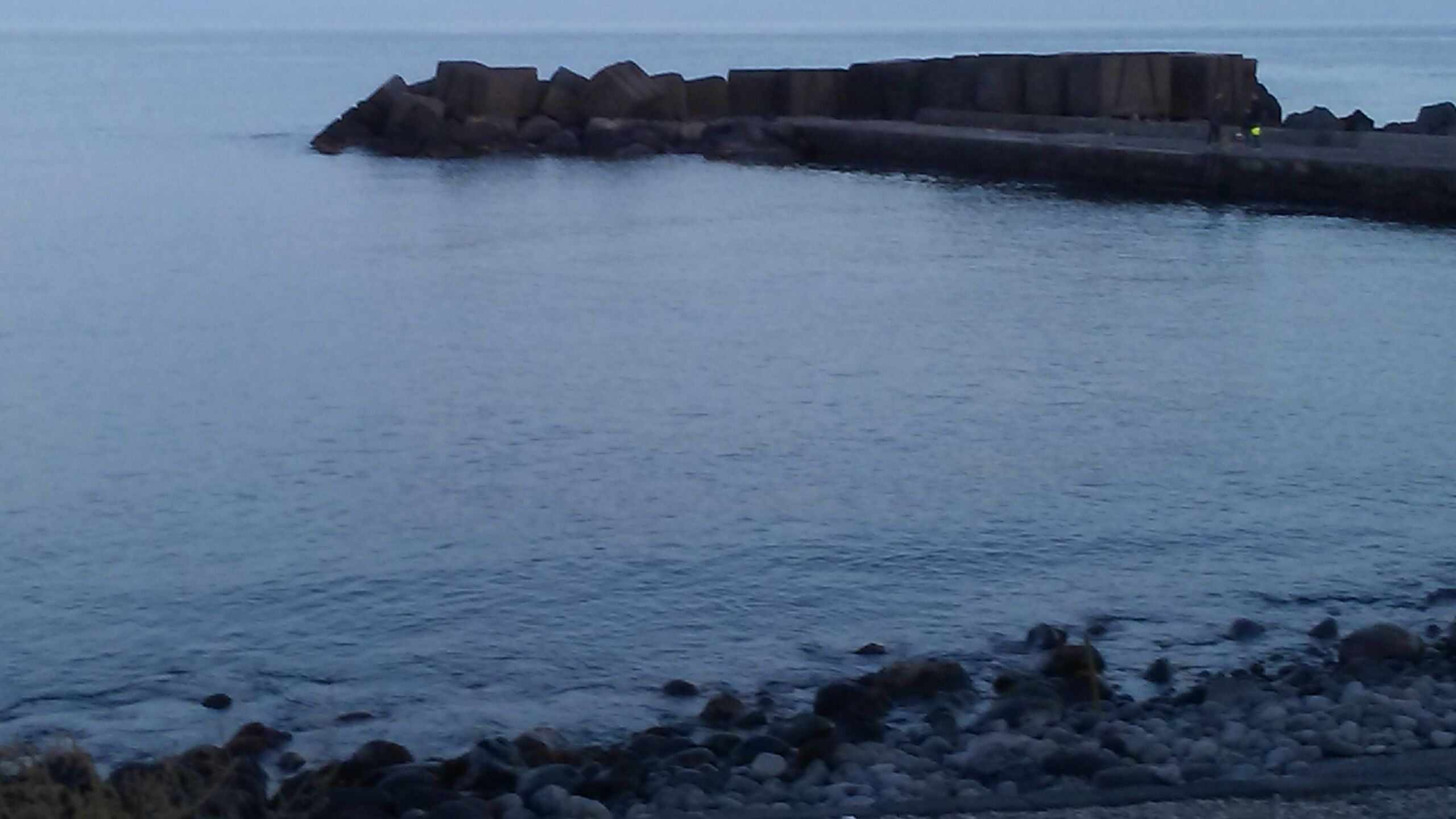 A coastal scene with a rocky breakwater extending into calm waters.