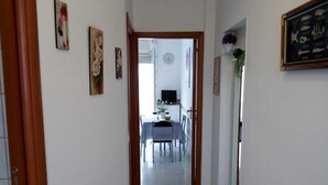 Ein Flur, der in einen Essbereich mit Tisch und Stühlen führt, mit einer Uhr an der Wand und einem gerahmten Bild.