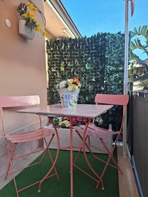 A small outdoor patio with a table and chairs, a potted plant, and a decorative wall.