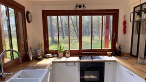 Uma cozinha com uma janela grande, uma pia, um forno e armários brancos.