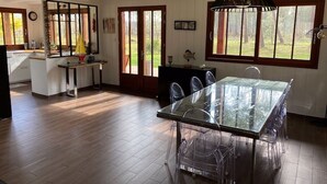 Cozinha espaçosa com mesa de jantar de vidro, piso de madeira e janelas amplas com vista para o exterior.