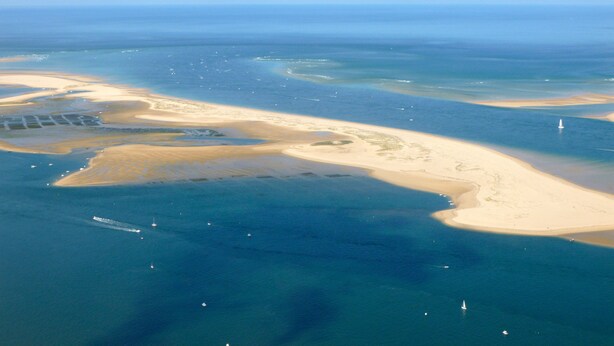 Vista aérea de uma área costeira com praias de areia e águas azul-claras.