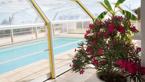 A pool area with a glass-enclosed structure and a potted plant with pink flowers. - House with all mod cons, covered and shared pool - quiet and green setting (Loubers)