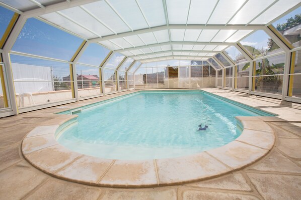 Una piscina interior con cerramiento de vidrio, agua azul cristalina y suelo de baldosas.