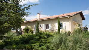 A two-story house with a tiled roof, surrounded by dense greenery and a stone wall. - House with all mod cons, covered and shared pool - quiet and green setting (Loubers)