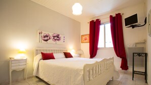 A bedroom with a white bed, red curtains, a mounted TV, and a bedside table with a lamp. - House with all mod cons, covered and shared pool - quiet and green setting (Loubers)