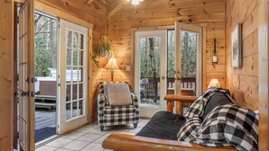 Ein gemütliches Cabin-Interieur mit einem karierten Sofa, einem Deckenventilator aus Holz und Blick ins Freie durch große Glasüren.