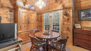 Ein Holzblockhaus-Interieur mit Esstisch, Stühlen, einem Kühlschrank und einem großen Fenster.