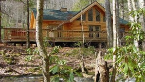Eine Blockhütte mit einer großen Terrasse und einem Fluss im Vordergrund.