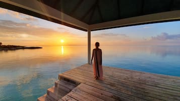 A person standing on a wooden deck overlooking a calm sea at sunset.