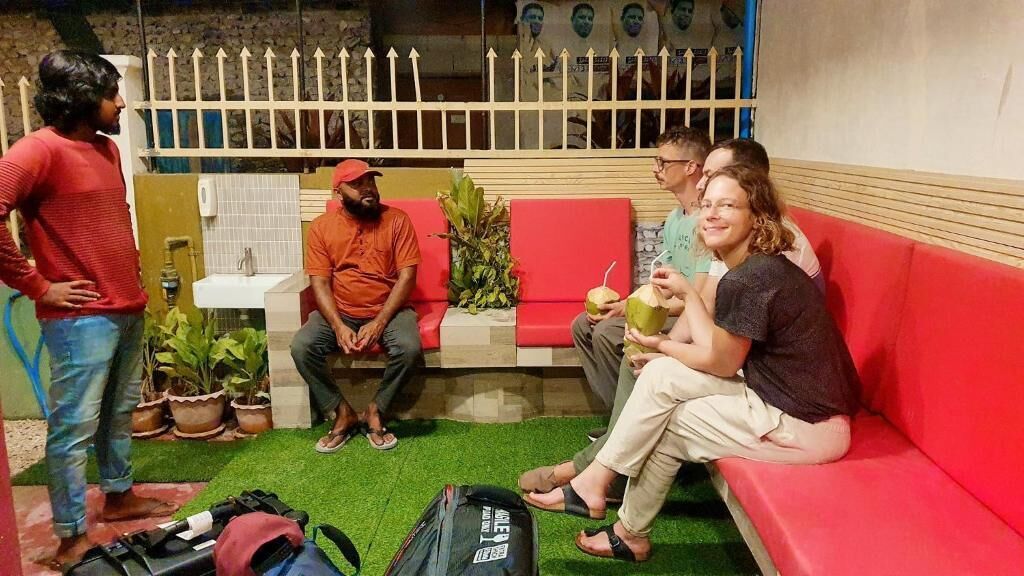 A group of people sitting on a red couch in a room with a white fence, potted plants, and a small table.