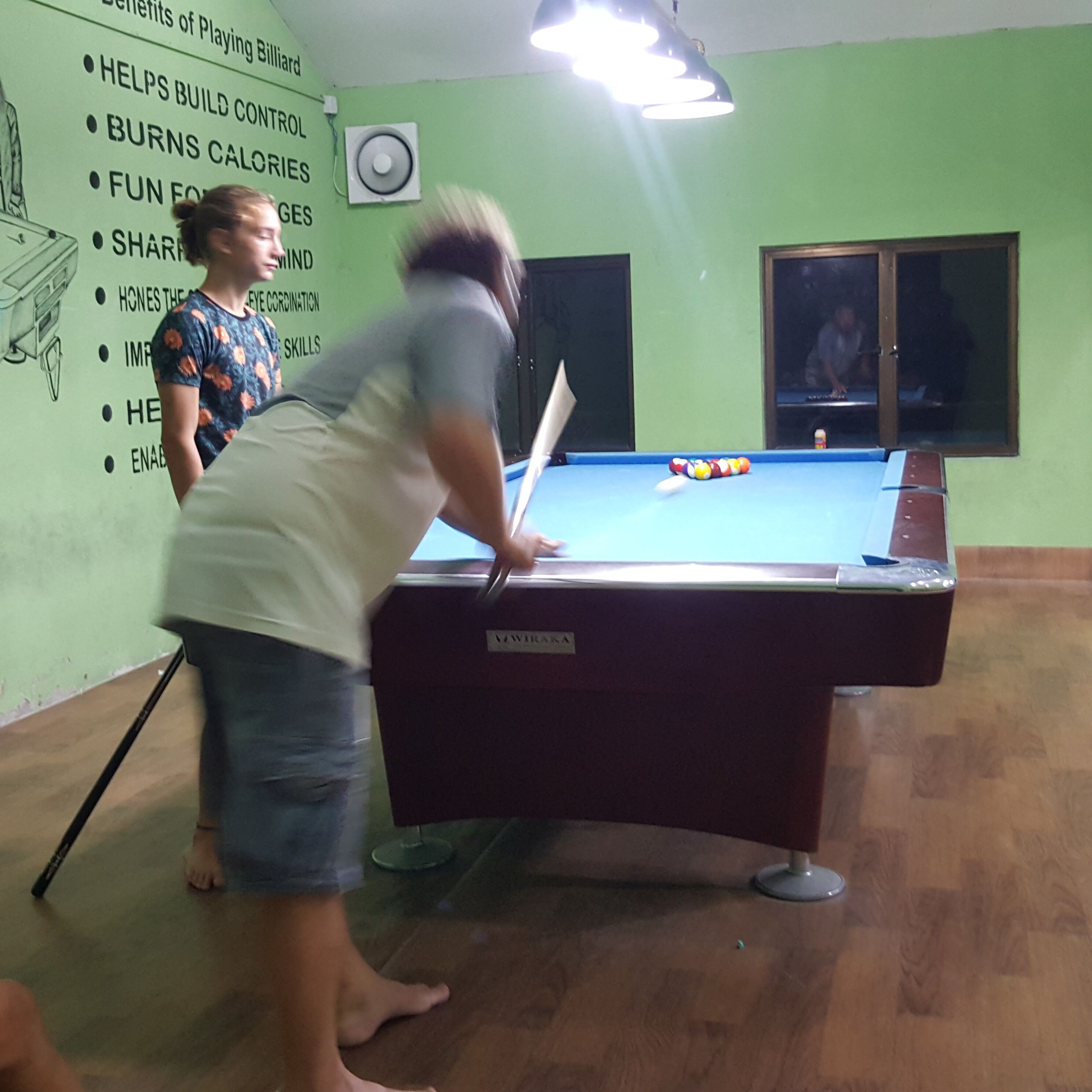 Una mesa de billar en una habitación con paredes verdes y un cartel que enumera las ventajas de jugar al billar.