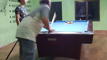 Una mesa de billar en una habitación con paredes verdes y un cartel que enumera las ventajas de jugar al billar.