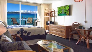 Een hotelkamer met een groot bed, een bureau, een stoel, een televisie en uitzicht op de oceaan.