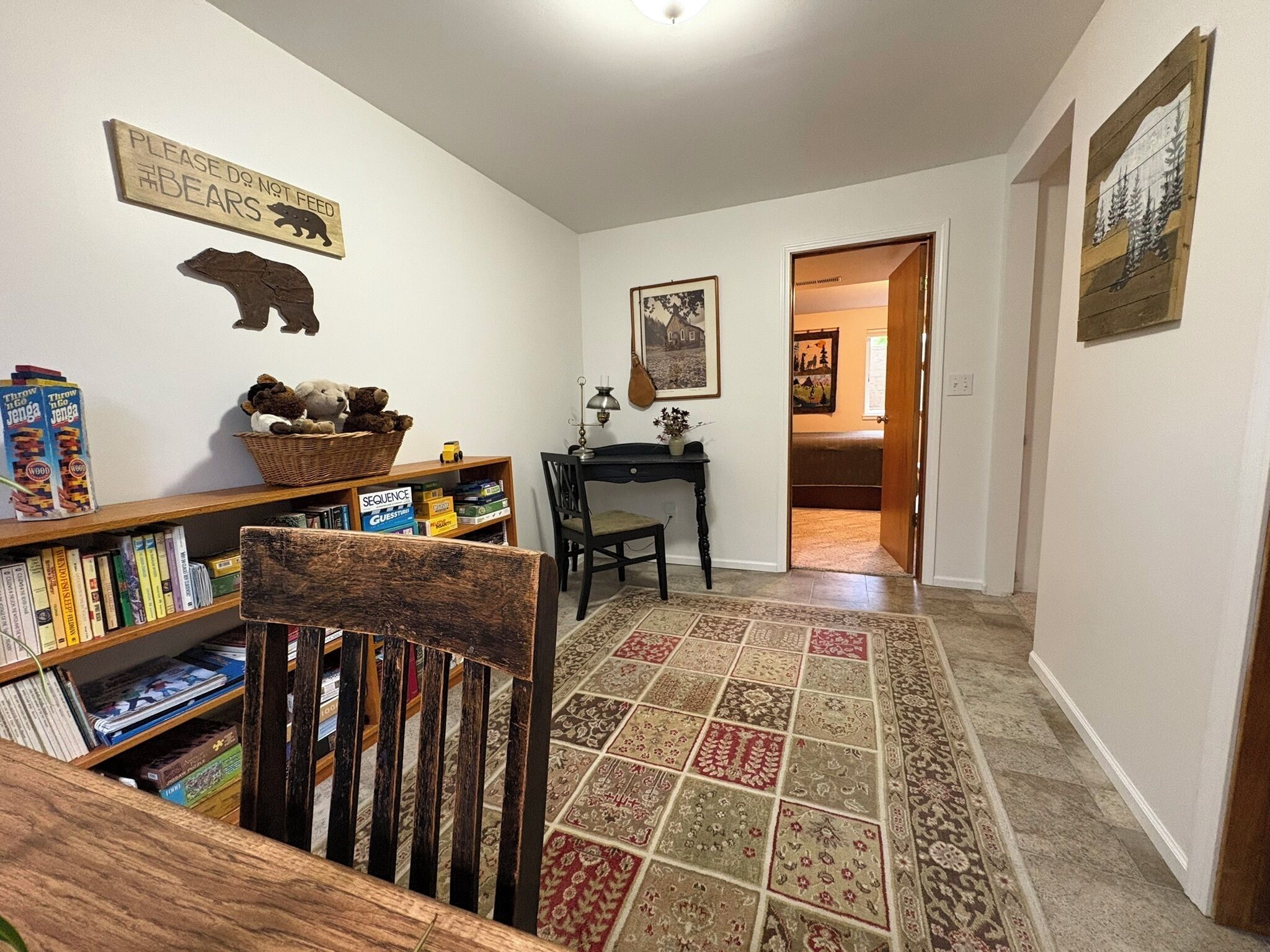 A cozy living room with a bookshelf, a wooden chair, a rug, and a door leading to another room.