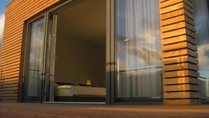 Um edifício moderno com uma ampla porta de correr de vidro que dá para um quarto com uma cama e uma mesa de cabeceira.