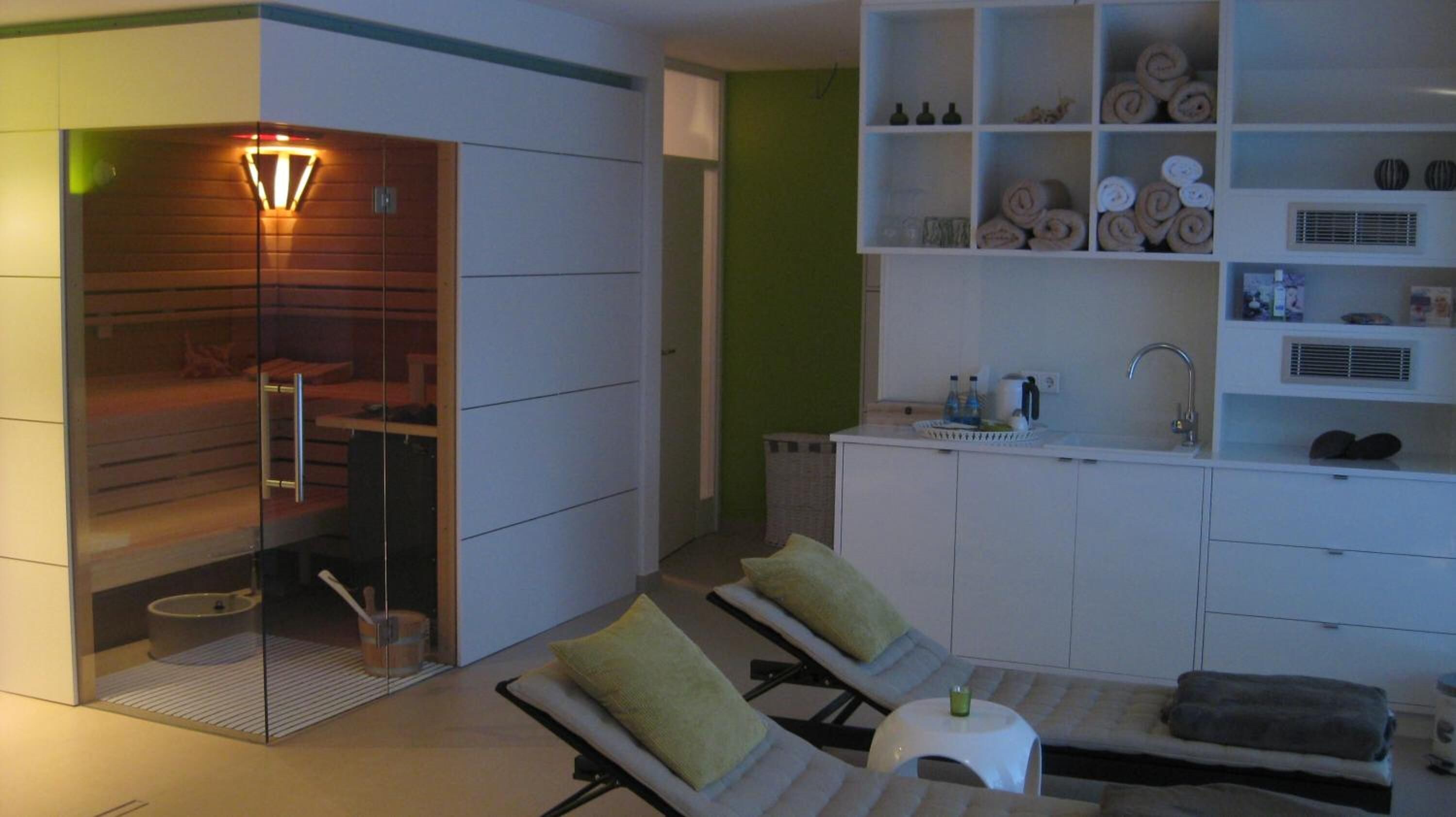 Un baño moderno con ducha de vidrio, lavamanos y una pequeña zona de estar con cojines.