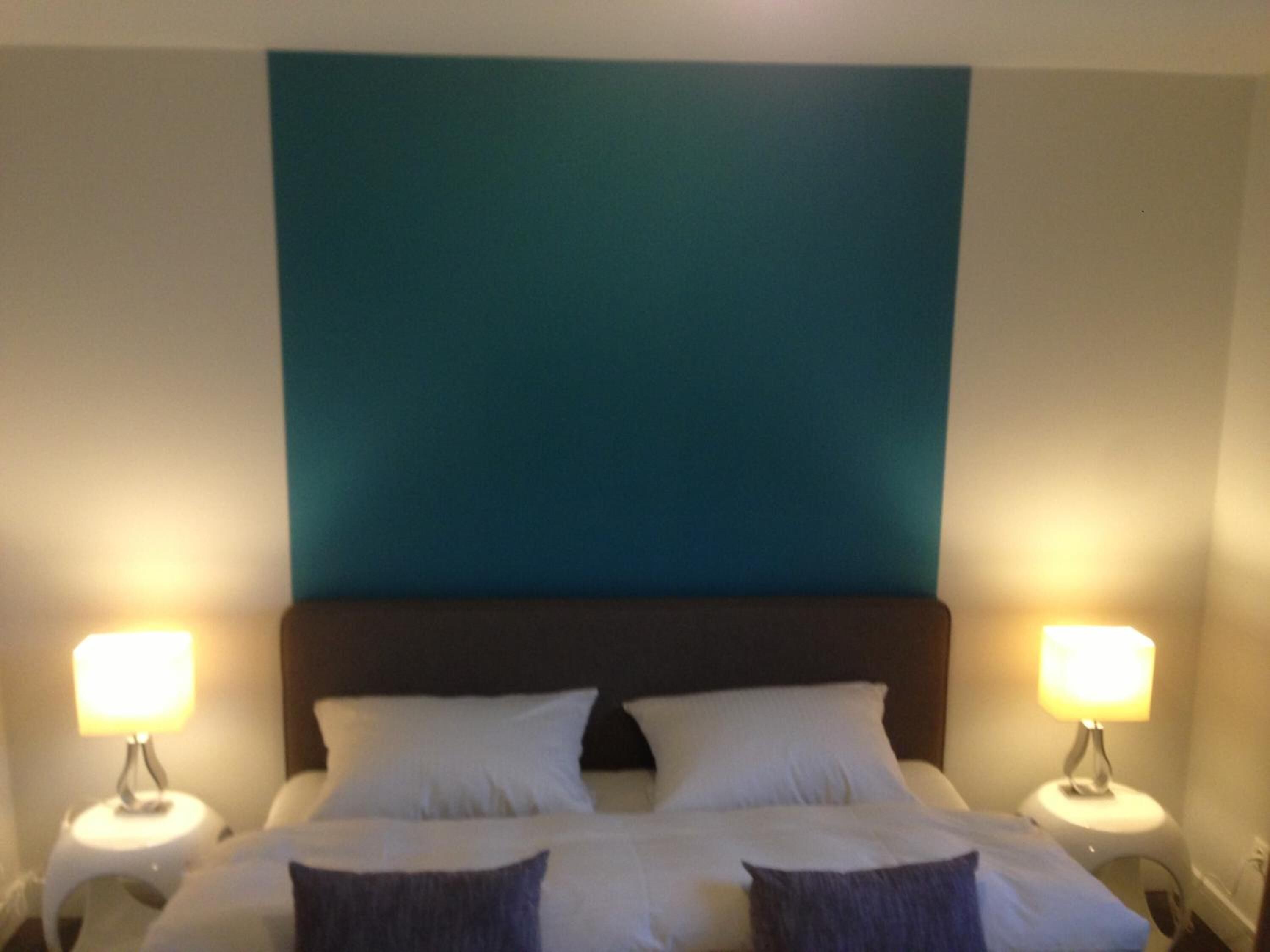 Ein Hotelzimmer mit einem großen Bett, zwei Nachttischlampen und einer Wand in Türkis.