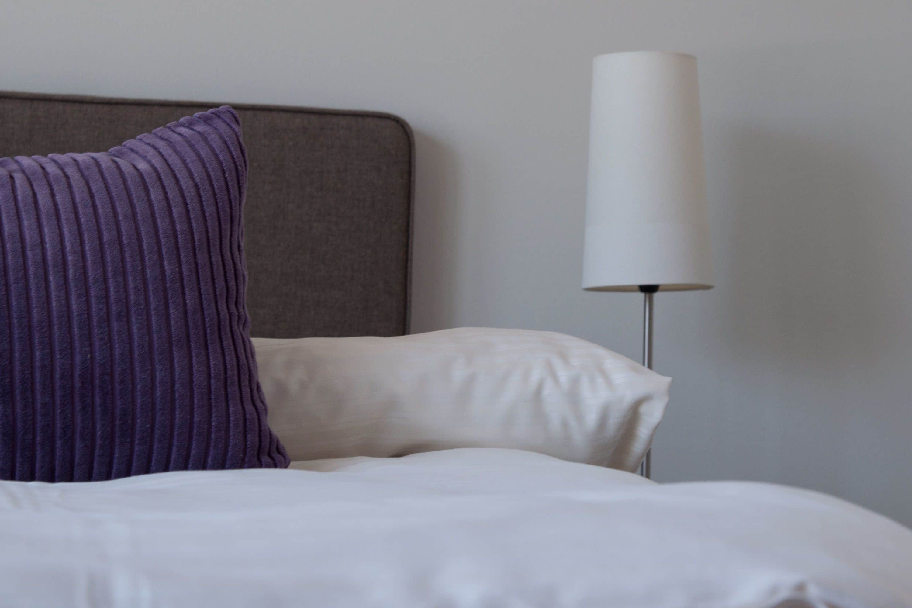 Una cama bien hecha con sábanas blancas y una almohada morada.
