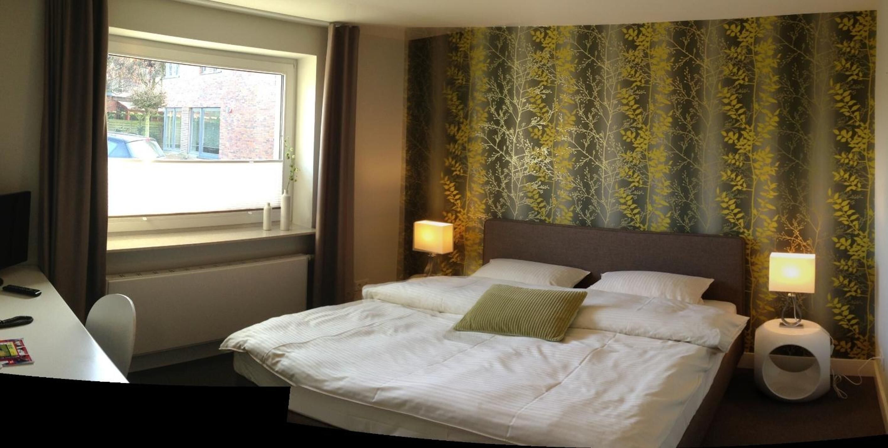 Ein Hotelzimmer mit Bett, zwei Nachttischlampen, einem Fenster und Blick nach draußen.