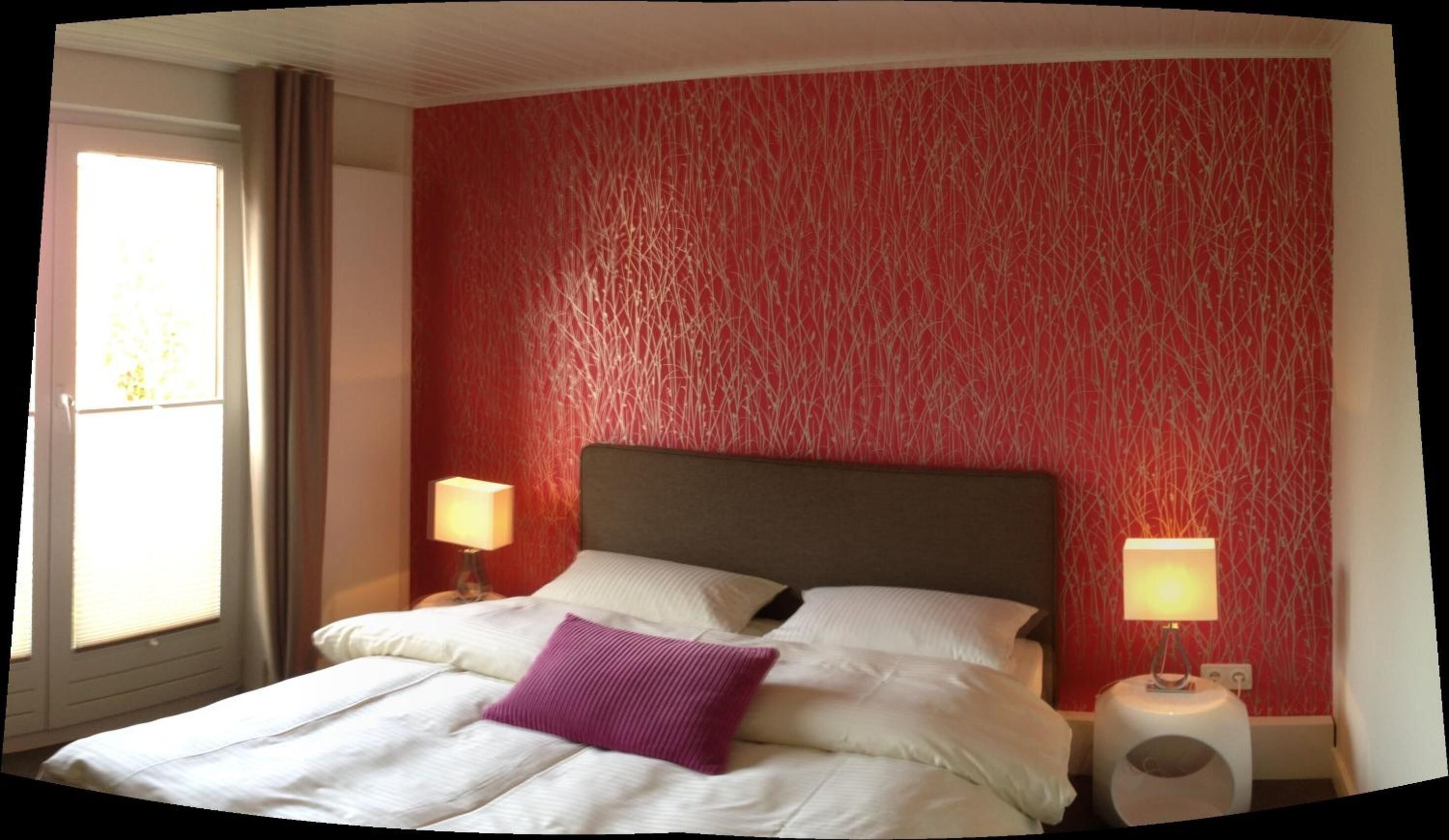 Quarto de hotel com uma cama grande, duas luminárias laterais e uma janela com cortinas.