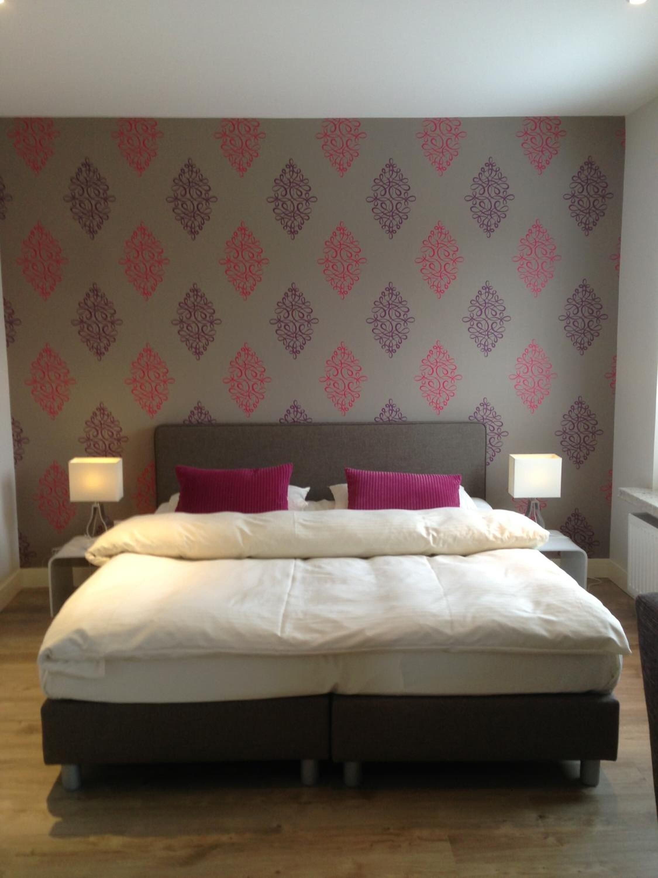 A double bed with two pillows, a nightstand with a lamp, and a patterned wallpaper.