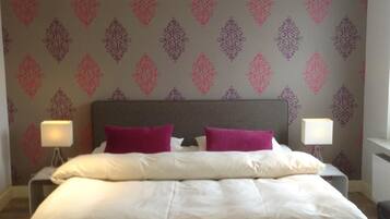 A double bed with two pillows, a nightstand with a lamp, and a patterned wallpaper.