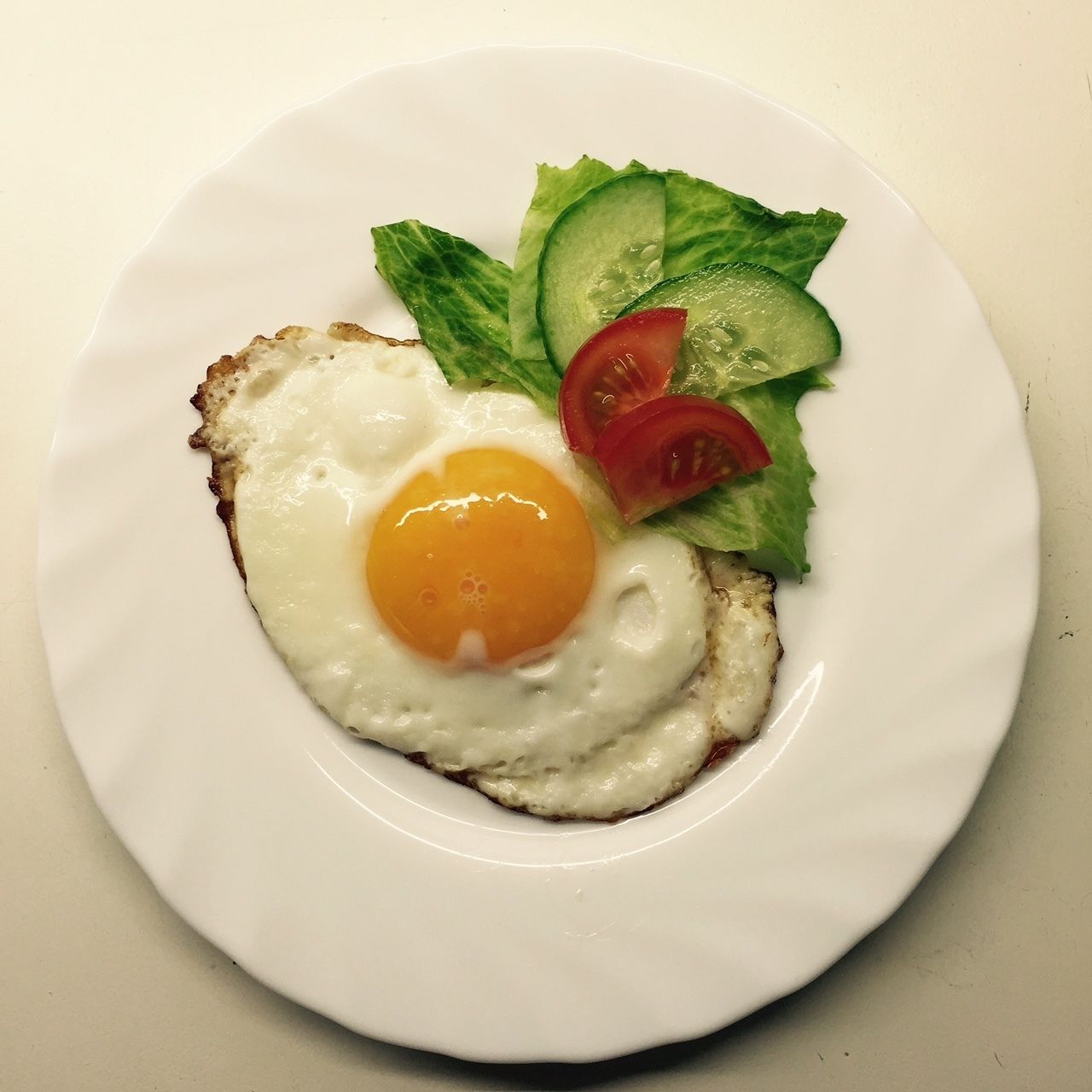 A plate with a fried egg, lettuce, and tomato slices.