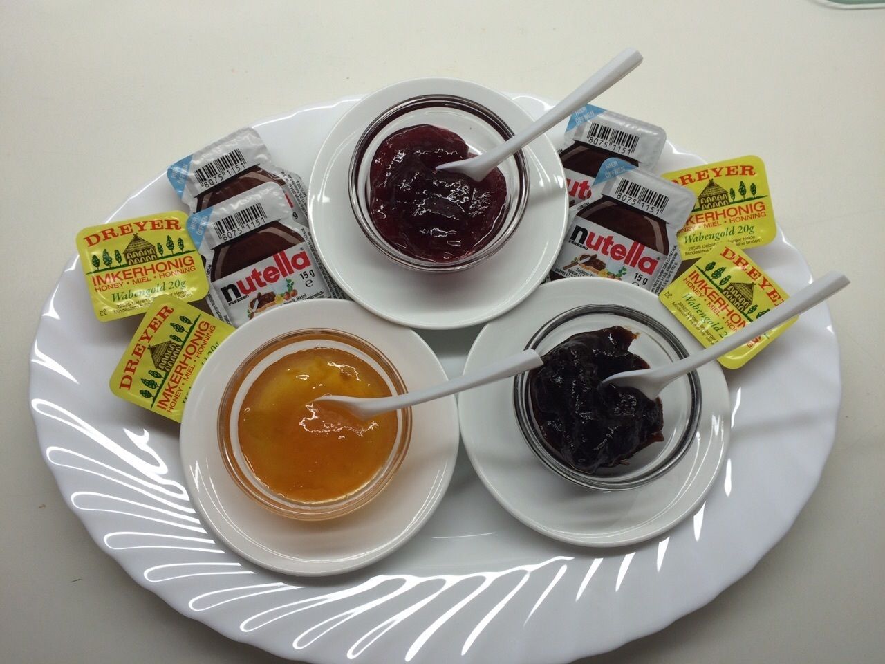 A plate with three jars of honey and two jars of Nutella.